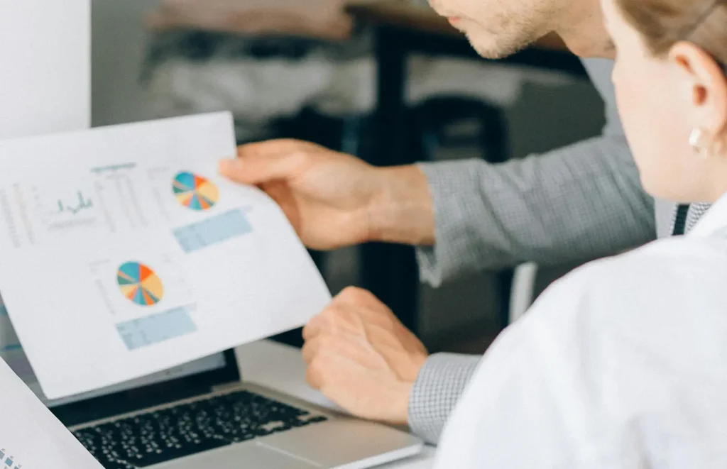 Två anonyma människor, en man och en kvinnar sitter och tillsammans tittar på en utskrift med grafer och statistik.