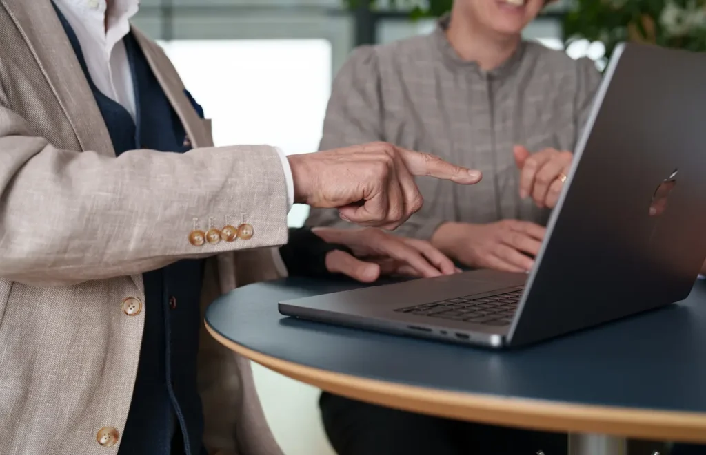 Två anonyma, professionellt klädda medarbetare sitter runt en dator och pekar mot skärmen.