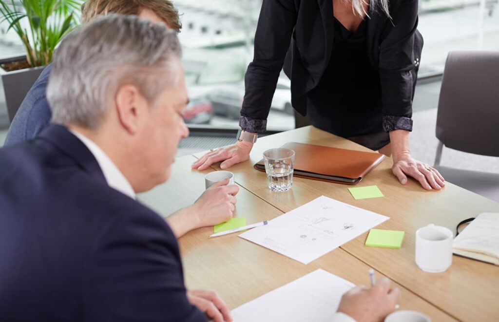 En grupp människor, en man och två kvinnor tittar på dokument som ligger på bordet framför dem.