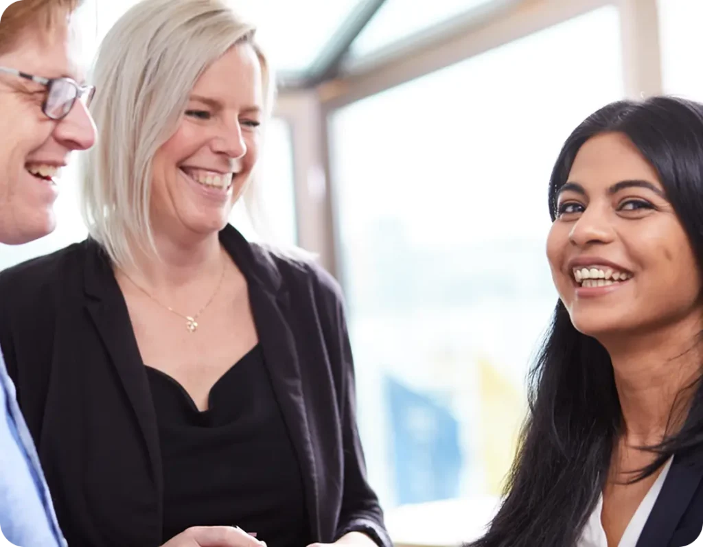 En man och två kvinnor, står leende mot varandra. En kvinnan tittar lite lätt mot kameran.