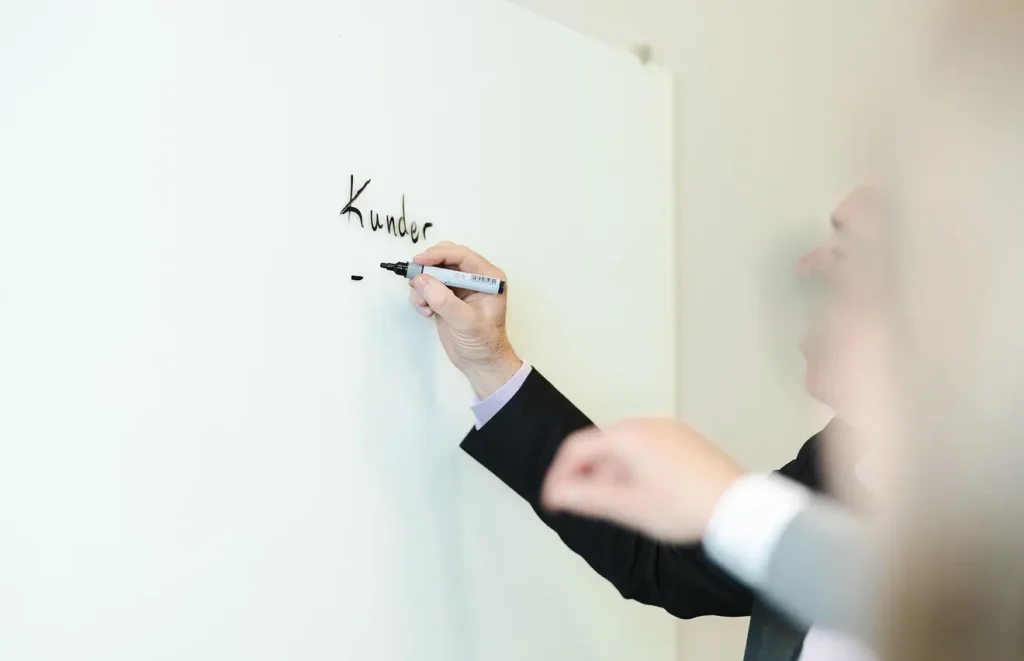 En anonym man, vars arm syns srikva på en whiteboard tavla. På tavlan står det "kunder." Ytterligare en hand syns i bild och verkar agera med mannen.