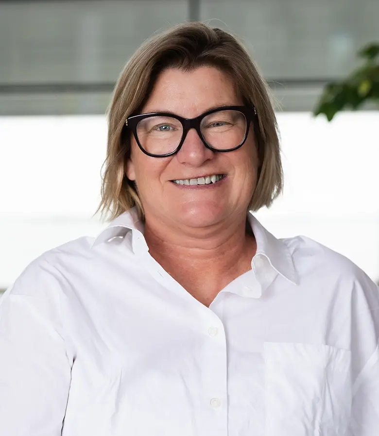 Ett personporträtt på en medelålders kvinna med skjorta och glasögon. Hon ler stort.